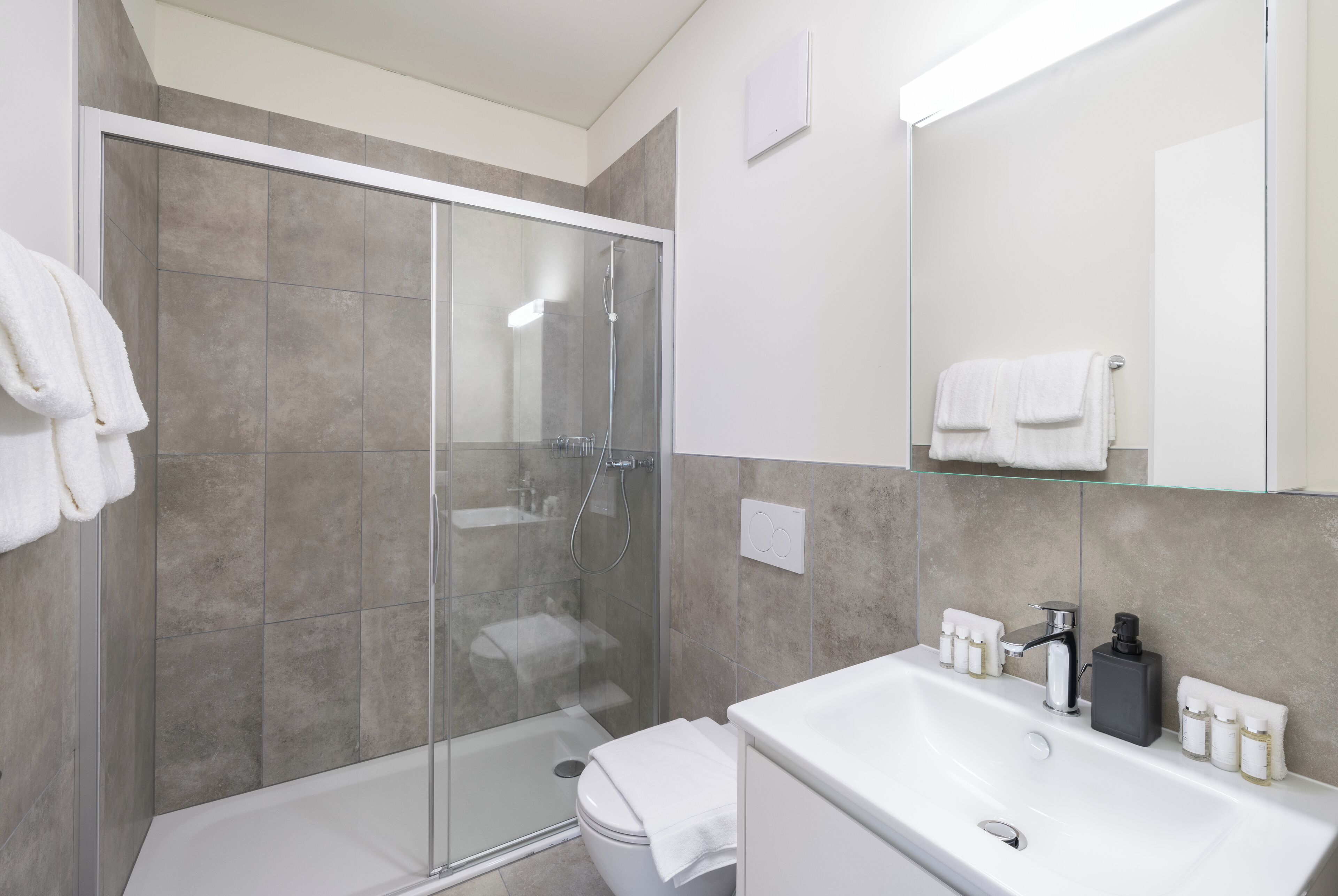 A modern bathroom with a glass shower enclosure, a white bathtub, and a large mirror above the sink.