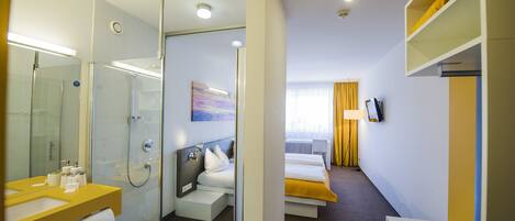 Una habitación de hotel moderna con ducha, lavabo, cama, televisor y mesita de noche.