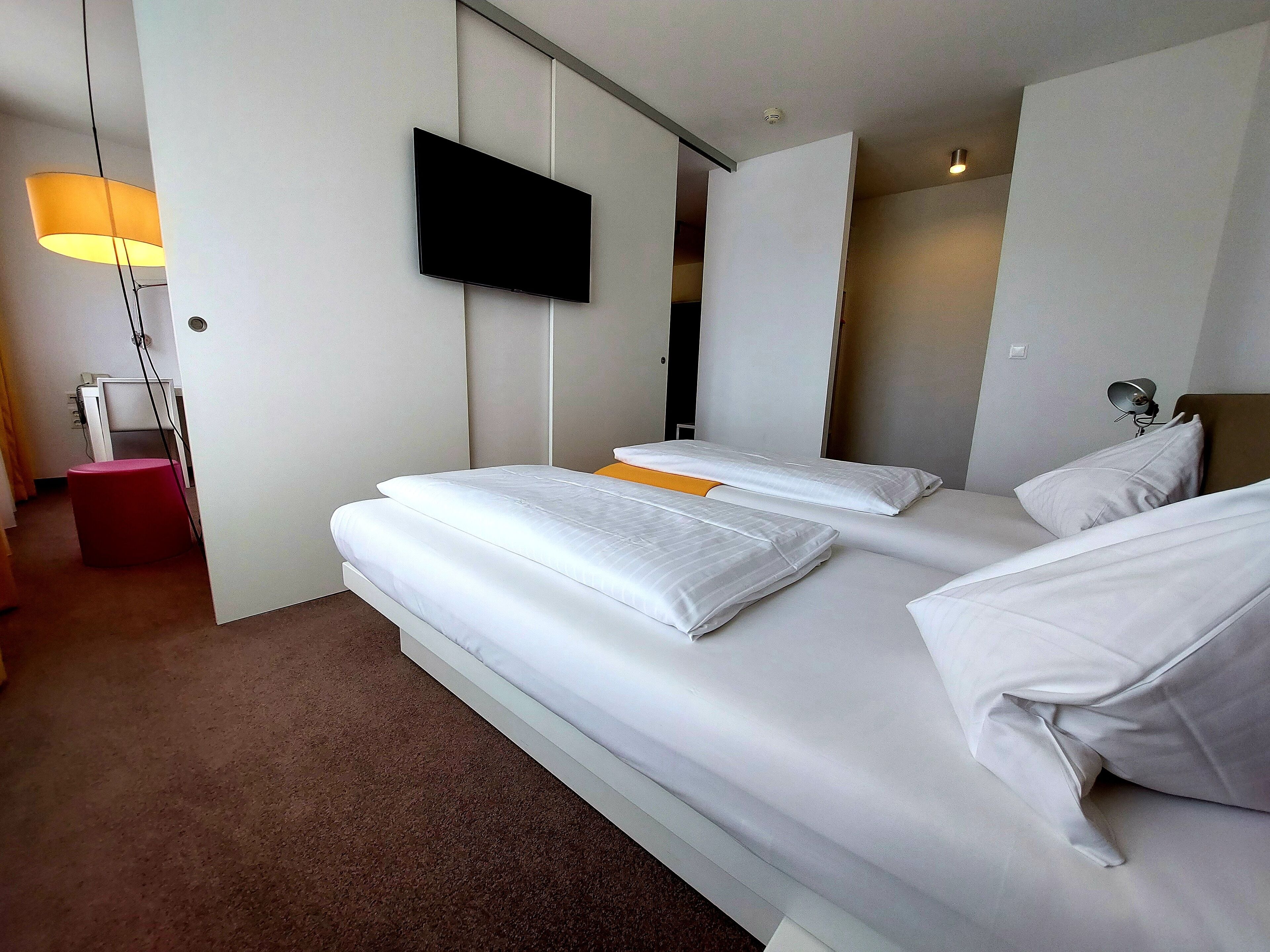 A hotel room with a large bed, a flat-screen TV mounted on the wall, and a bedside lamp.