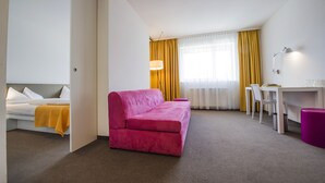 A hotel room with a pink sofa, a white bed, a desk, and a chair. - STAY.inn Comfort Art Hotel Schwaz (Schwaz)