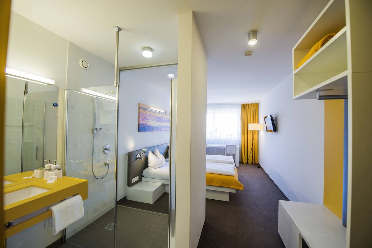 A hotel room with a shower, a bed, a bedside table, a TV, and a window with curtains.