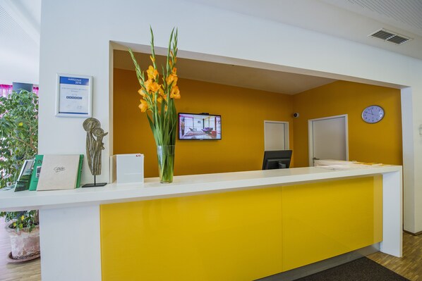 Un comptoir d’accueil avec un mur d’accent jaune, une horloge et un écran de télévision.