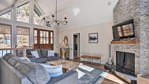 Een ruime woonkamer met een stenen open haard, grote ramen en een gezellige zithoek.
