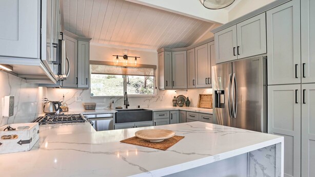 Een moderne keuken met grijze kastjes, een groot marmeren eiland, roestvrijstalen apparatuur en een raam met natuurlijk licht.