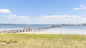 Un muelle que se adentra en aguas tranquilas, con un primer plano de césped y un cielo despejado.