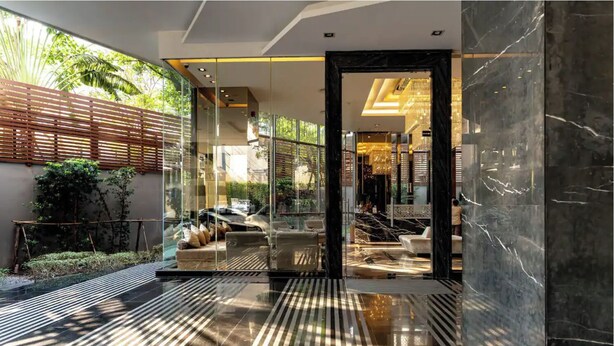 Un intérieur moderne avec un mur de verre, un coin salon doté de coussins et un sol en marbre.