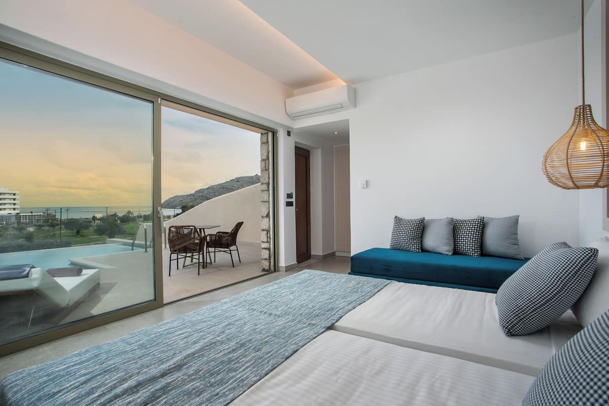 A modern living room with a sofa, a dining area with chairs, and a large sliding glass door leading to a balcony with a view of a cityscape.