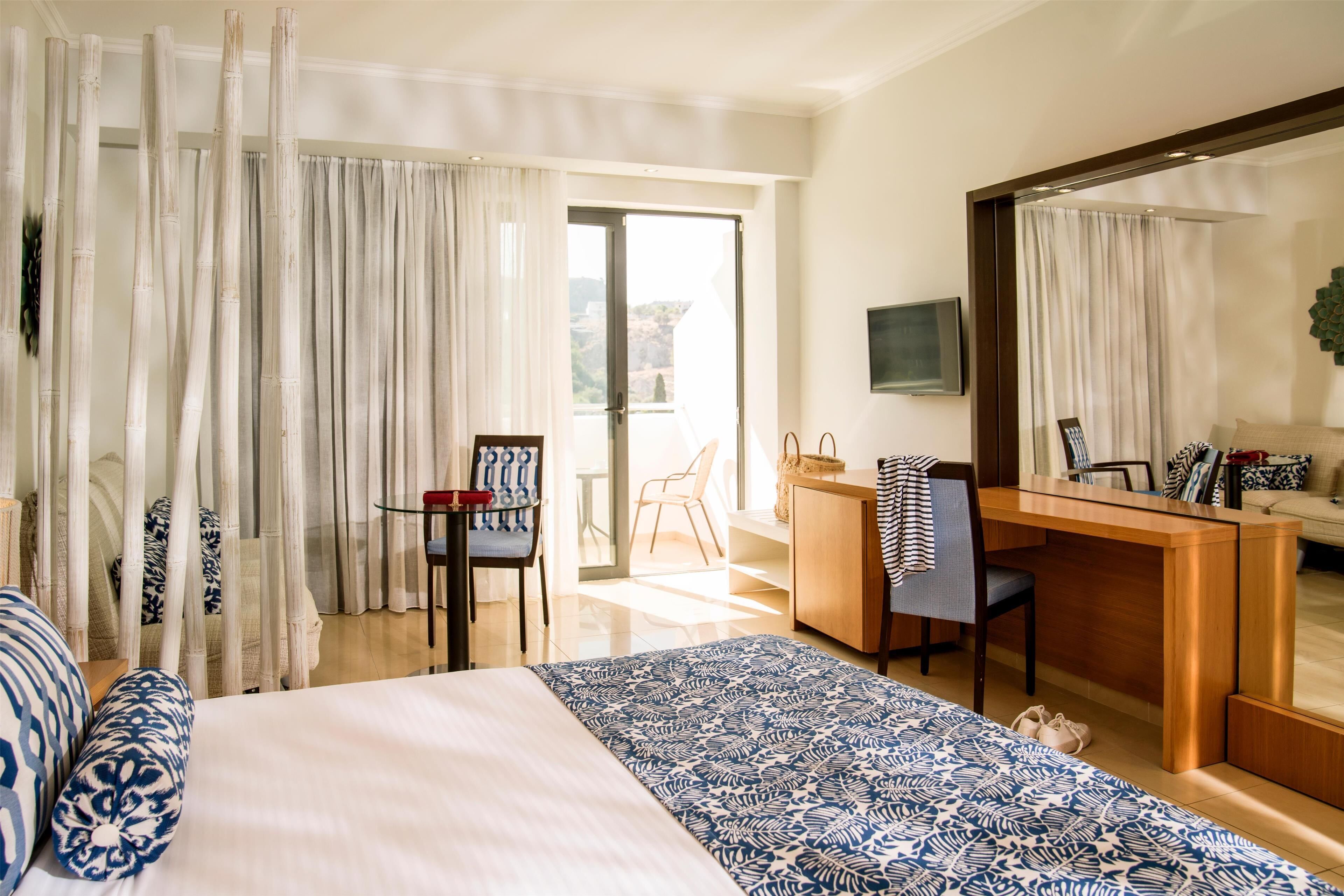 A hotel room with a bed, a desk, a chair, a television, and a balcony with curtains.