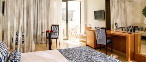 A hotel room with a bed, a desk, a chair, a television, and a balcony with curtains.