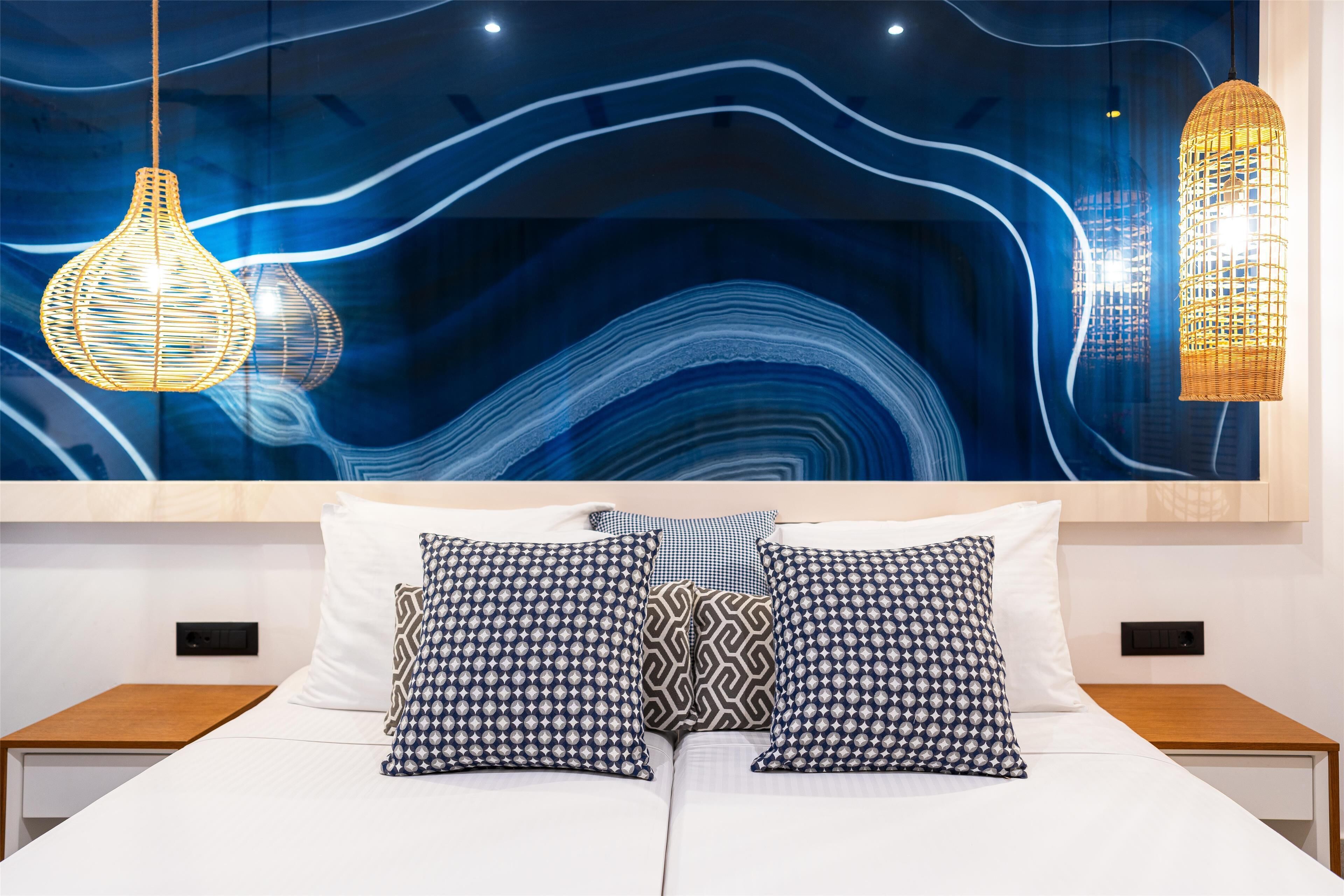 A modern hotel room with a large abstract wall art, two bedside tables, and patterned pillows.