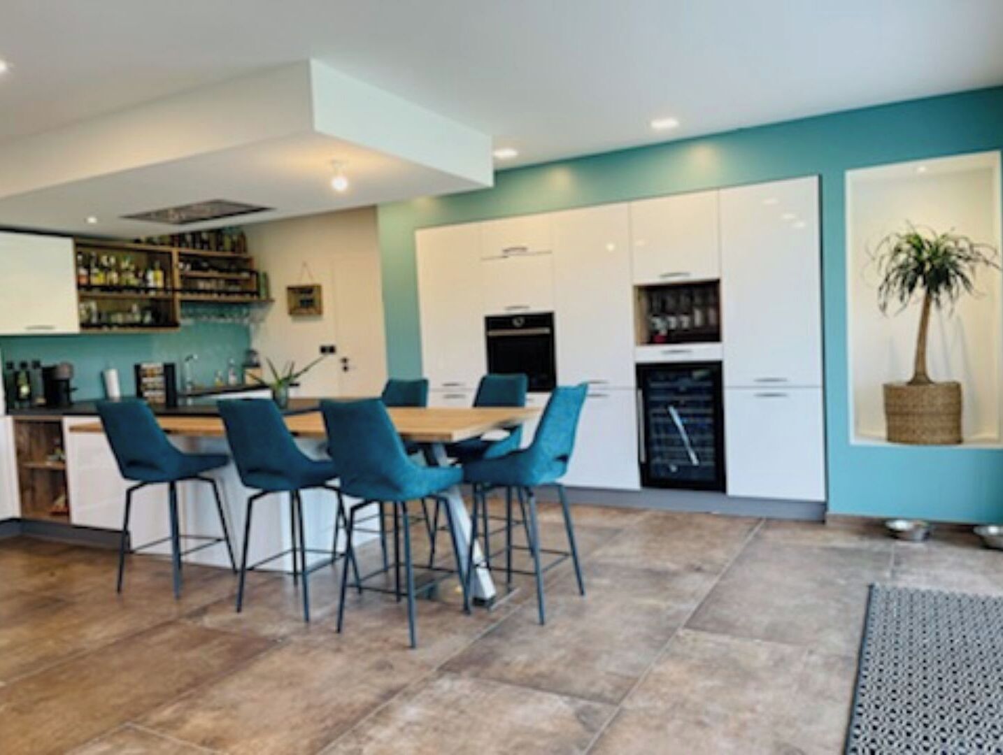 Une cuisine moderne avec des meubles blancs, une table à manger entourée de chaises bleues et une plante en pot.