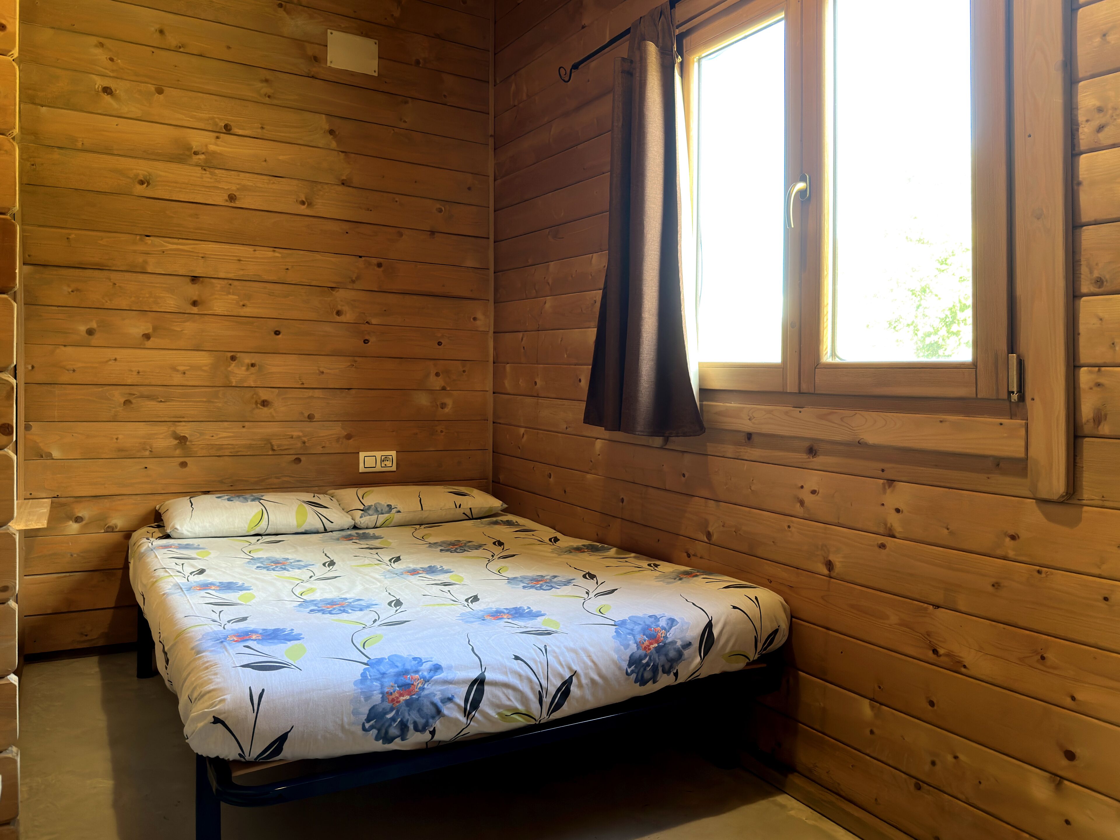 Une pièce de cabane en bois comprenant un lit, une fenêtre avec des rideaux et un mur en bois.