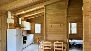A wooden cabin with a kitchen, dining area, and a bed. - Camping Rural Montori (Ultramort)