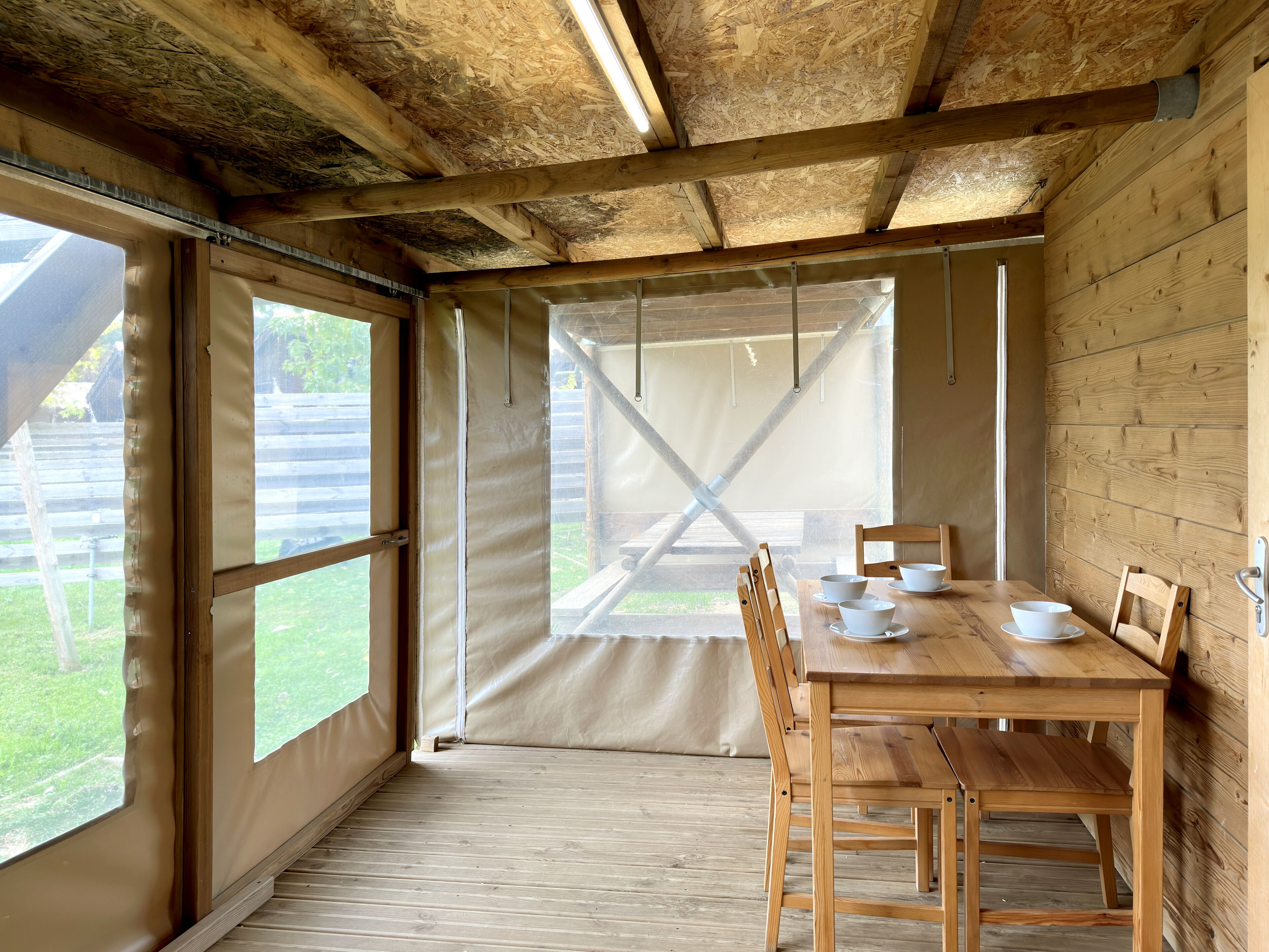 A wooden interior with a table set for dining, large windows, and a view of the outdoors.