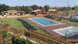 A pool area with lounge chairs, wooden cabins, and a playground. - Camping Rural Montori (Ultramort)
