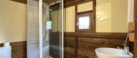 Ein Badezimmer einer Holzhütte mit einer gläsernen Duschkabine, einem weißen Waschbecken und einer Toilette.