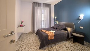 A bedroom with a bed, a bedside table, a nightstand, a window with curtains, a wall-mounted light, and a door. - Neva-Elegant Suite with Balcony in Massa Lubrense center 10 minutes from Sorrento (Massa Lubrense)