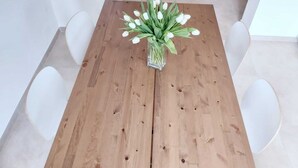 Una mesa de madera para comer con un jarrón de tulipanes blancos en el centro, rodeada de sillas blancas.