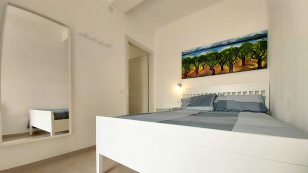 Un dormitorio con una cama grande, una mesita de noche, un cuadro de un paisaje y un espejo en la pared.