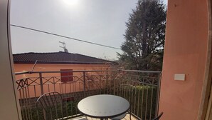 Un balcón con una mesa redonda y dos sillas, baranda de metal y vista a un edificio con tejado de tejas.