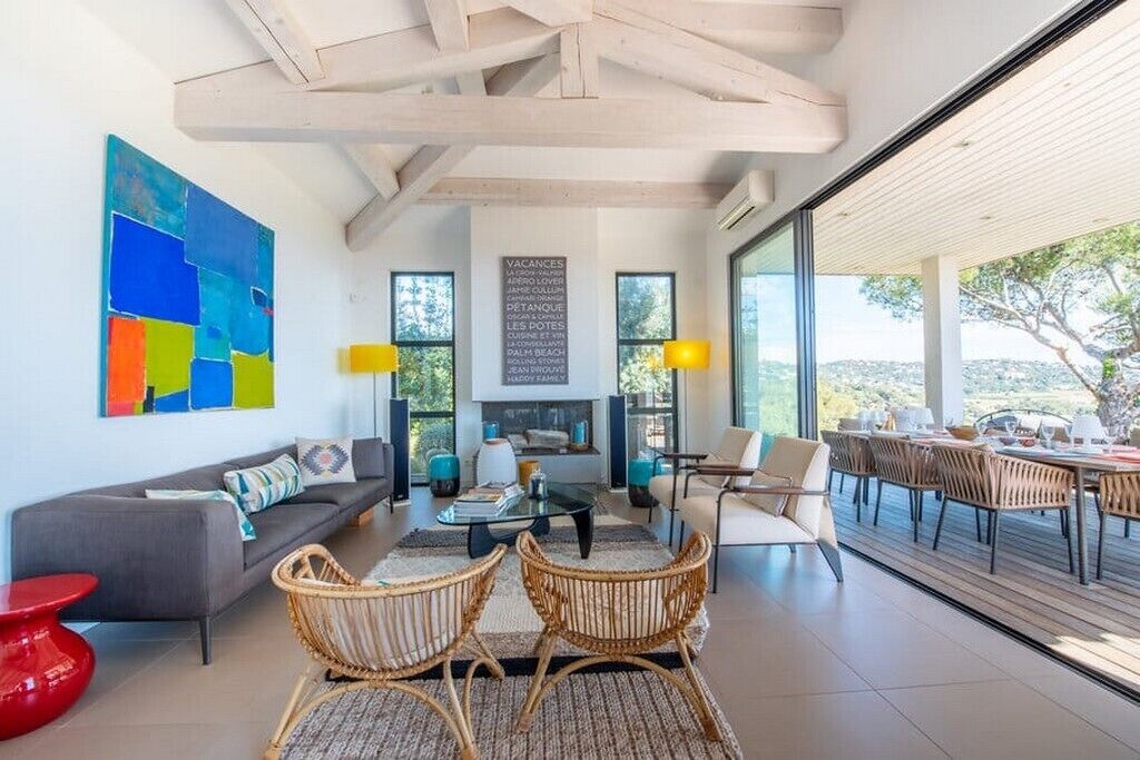 A modern living room with a sofa, coffee table, and wicker chairs. There is a large window with a view of the outdoors.