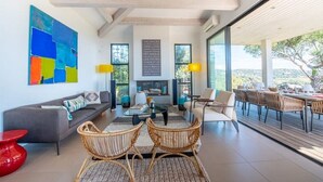 A modern living room with a sofa, coffee table, and wicker chairs. There is a large window with a view of the outdoors.