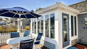 A covered patio with a table and chairs, a blue umbrella, and a small garden area.