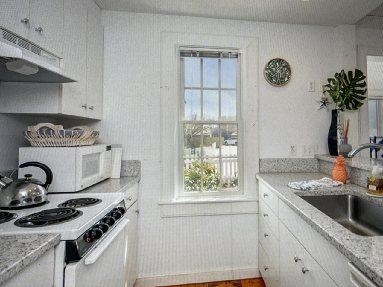 A compact kitchen with white cabinetry, a built-in microwave, a stove, and a sink.