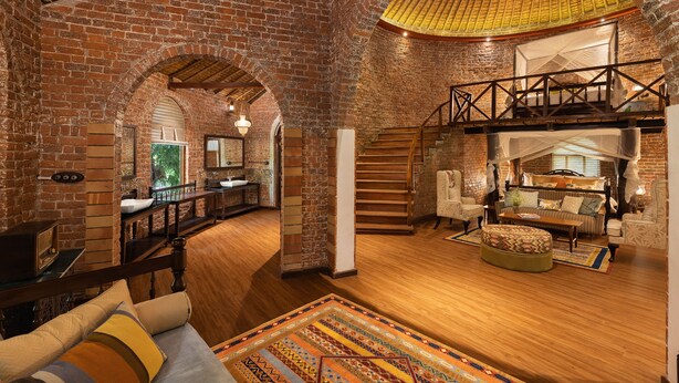 Een ruime loft met blootliggende bakstenen muren, een houten trap en een gezellige zithoek met een kamerkleed.