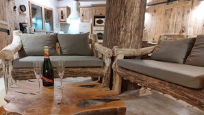 A rustic wooden sofa with cushions, a wooden coffee table, and a bottle of champagne. - Le Cul de Loup, self-catering cottage (Crouy-sur-Cosson)