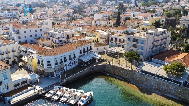 Une ville côtière aux bâtiments blancs, dotée d’un mur de pierre et où des bateaux sont amarrés dans le port.