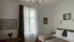 Ein Hotelzimmer mit Bett, Schreibtisch, Stuhl, einer Kandelaber und einem fensterbepflanzten Fenster.