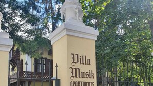 Ein Gebäude mit der Aufschrift "Villa Musik Apartments", einem verschlossenen Eingangstor und einer Statue auf dem Dach.
