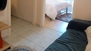 A bedroom with a bed, a bedside table, a rug, and a door leading to another room. - Cozy Studio at Kallithea, Fully Equipped (Nea Smirni)