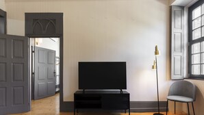 Ein Wohnzimmer mit einem schwarzen Unterhaltungsmöbel, einem gemusterten Teppich, einer hohen Stehlampe und einem grauen Sessel.