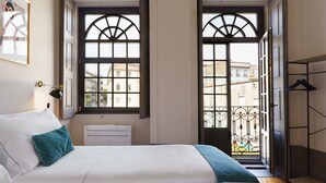 Habitación de hotel con cama, escritorio y vistas a la ciudad a través de amplias ventanas.