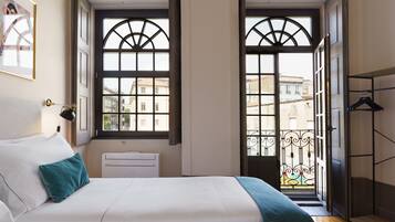 Een hotelkamer met een bed, een bureau en uitzicht op de stad door grote ramen.