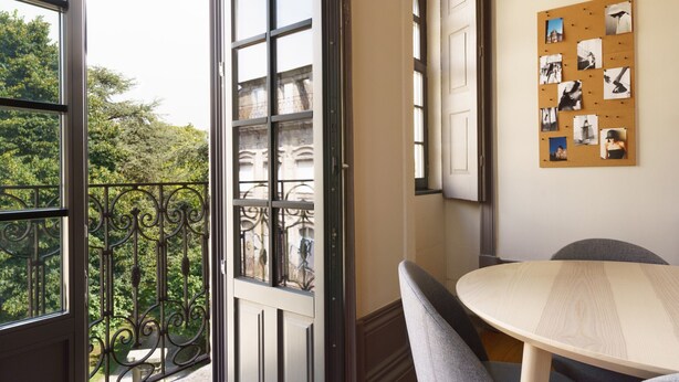Una habitación con balcón, un tablón de corcho con fotos y una mesa redonda.