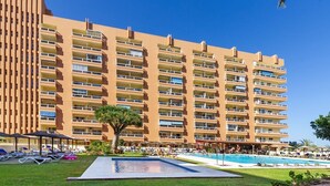 A multi-story hotel with balconies, a swimming pool, and a well-maintained lawn.