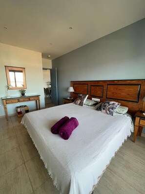 A bedroom with a large bed, a desk, a chair, and a mirror.