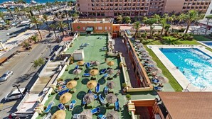 A hotel with a rooftop pool, lounge chairs, and a view of the sea.