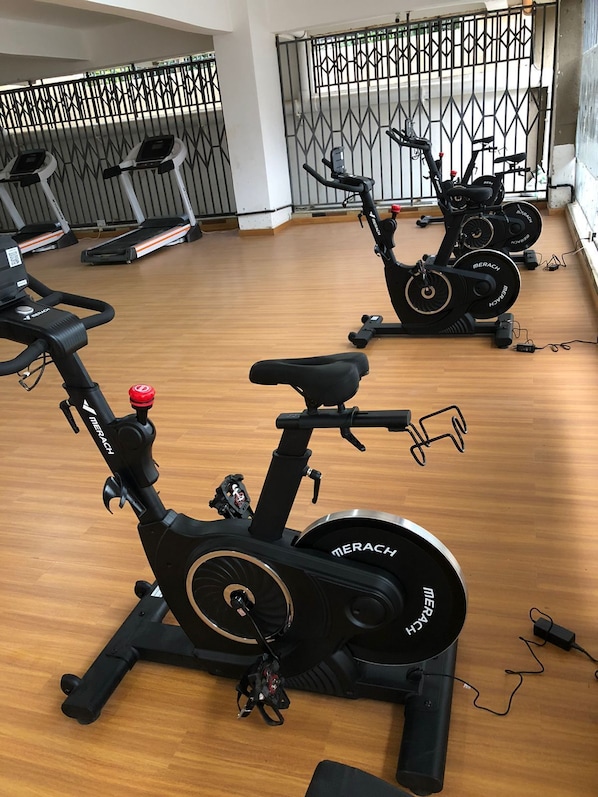 A gym with stationary bikes, a wooden floor, and a metal fence in the background.