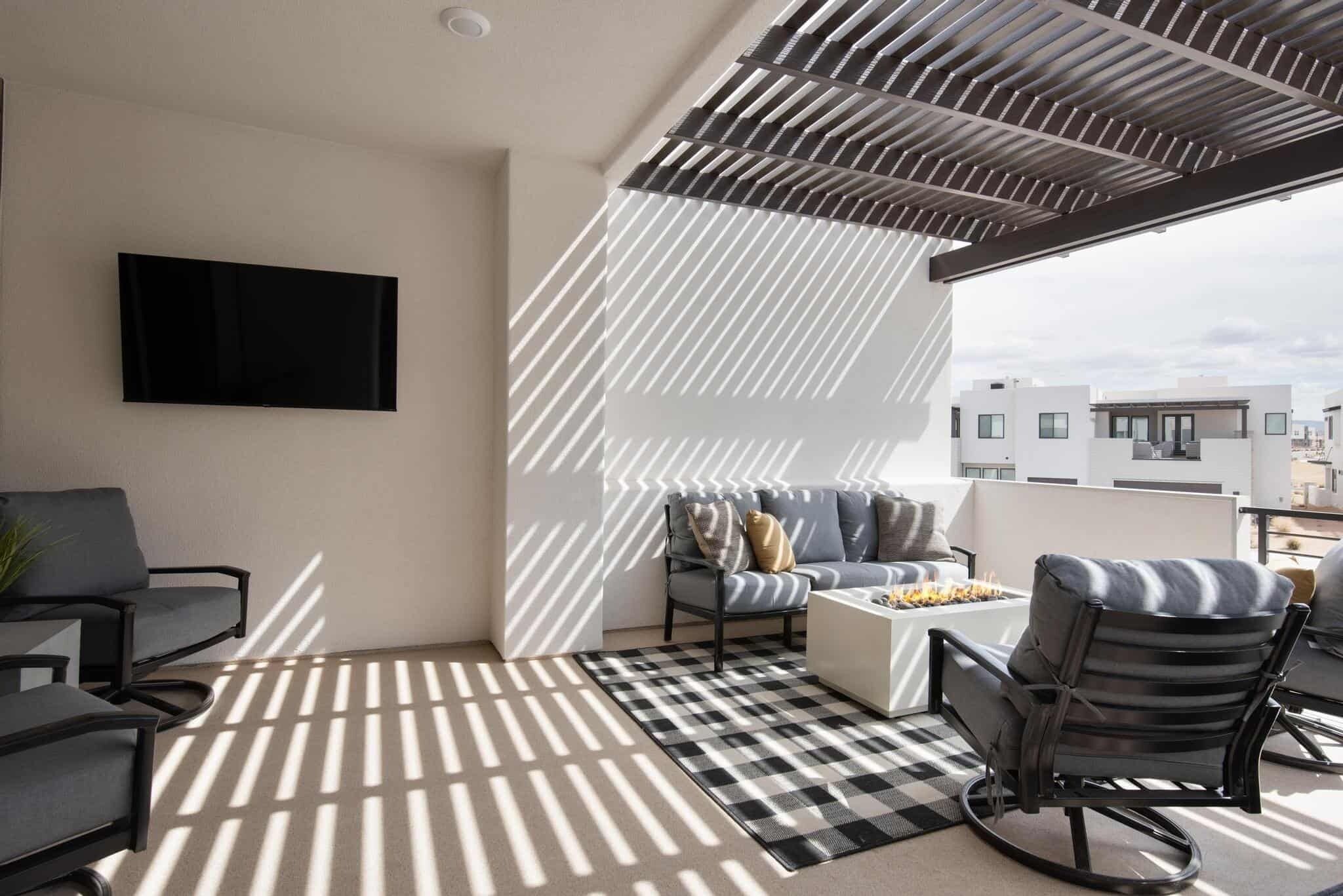 A balcony with a checkered floor, a sofa, a chair, and a TV mounted on the wall.