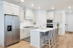 A modern kitchen with white cabinetry, stainless steel appliances, and a central island with bar stools.