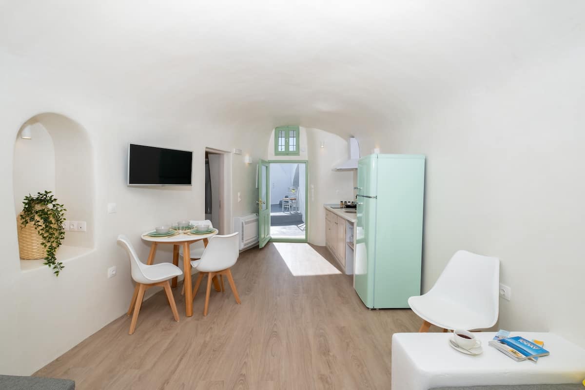 Cocina compacta con comedor, televisor montado en la pared y vistas a través de una puerta abierta.
