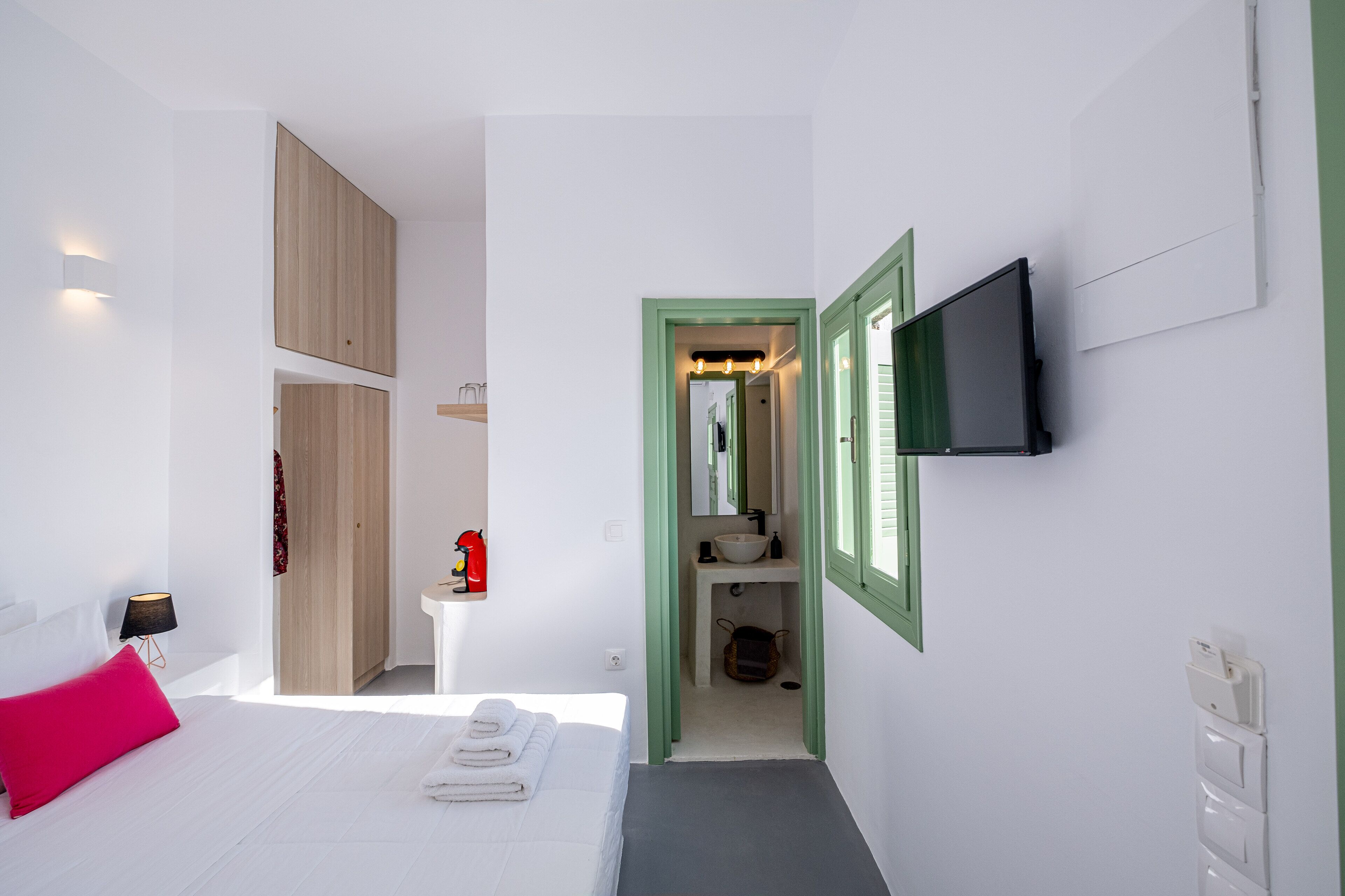 Ett modernt hotellrum med en säng, en tv som är monterad på väggen, ett litet sängbord och ett badrum som syns genom en öppen dörr.