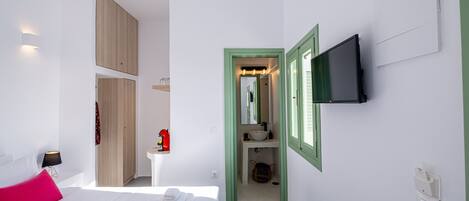 Ett modernt hotellrum med en säng, en tv som är monterad på väggen, ett litet sängbord och ett badrum som syns genom en öppen dörr.