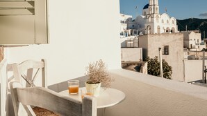 Un balcon avec une table blanche, une chaise, un pot de fleurs et deux verres de jus d’orange.