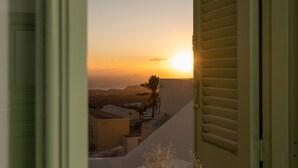 Une vue depuis une fenêtre avec volets, donnant sur un paysage côtier avec des bâtiments et un palmier au coucher du soleil.