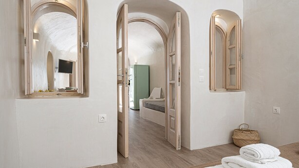 Une chambre d’hôtel avec un plancher en bois, un lit doté d’une tête de lit verte, un téléviseur fixé au mur et un panier tressé sur le côté.